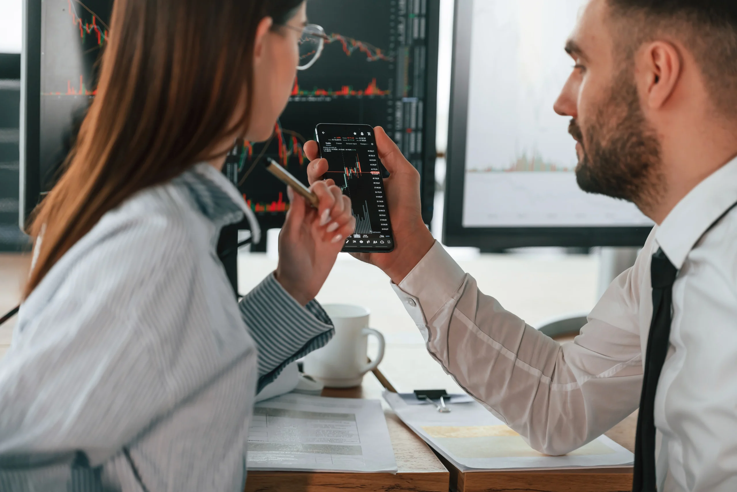 Man and woman analyzing Bitcoin price charts on a smartphone, discussing their first steps in buying cryptocurrency.