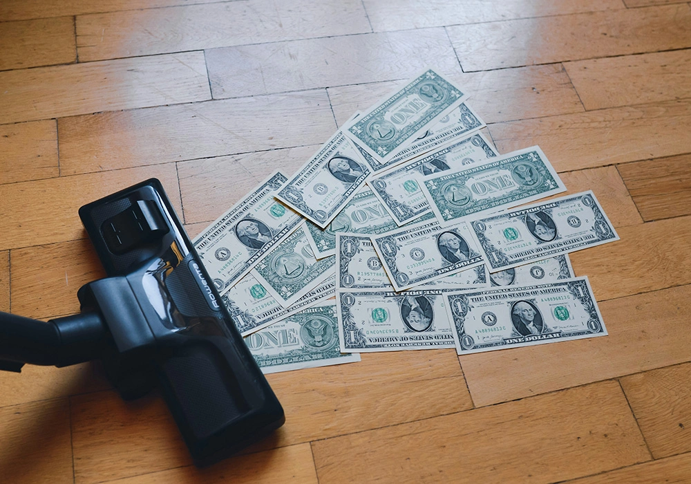 How Inflation Impacts Investments and Ways to Protect Your Wealth 2 Dollar bills scattered on floor next to vacuum cleaner symbolizing money loss or financial waste
